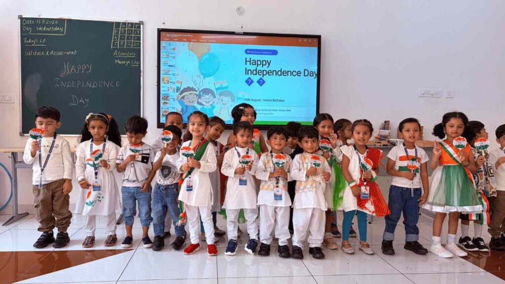 Pre-Primary children in patriotic outfits holding handcrafted Indian flag badges in a classroom.